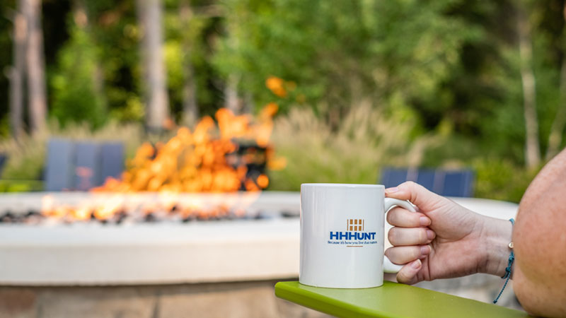 Hand holding a coffee mug near a fire pit